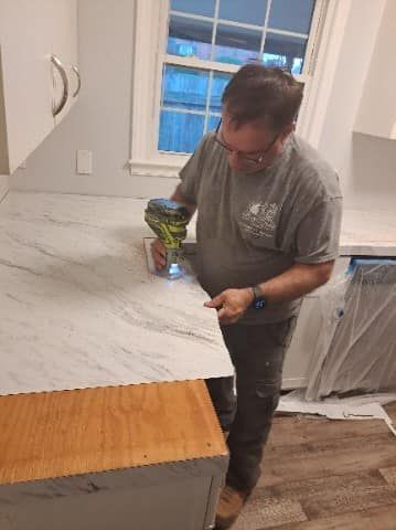 A person uses a power tool on a countertop in a kitchen.