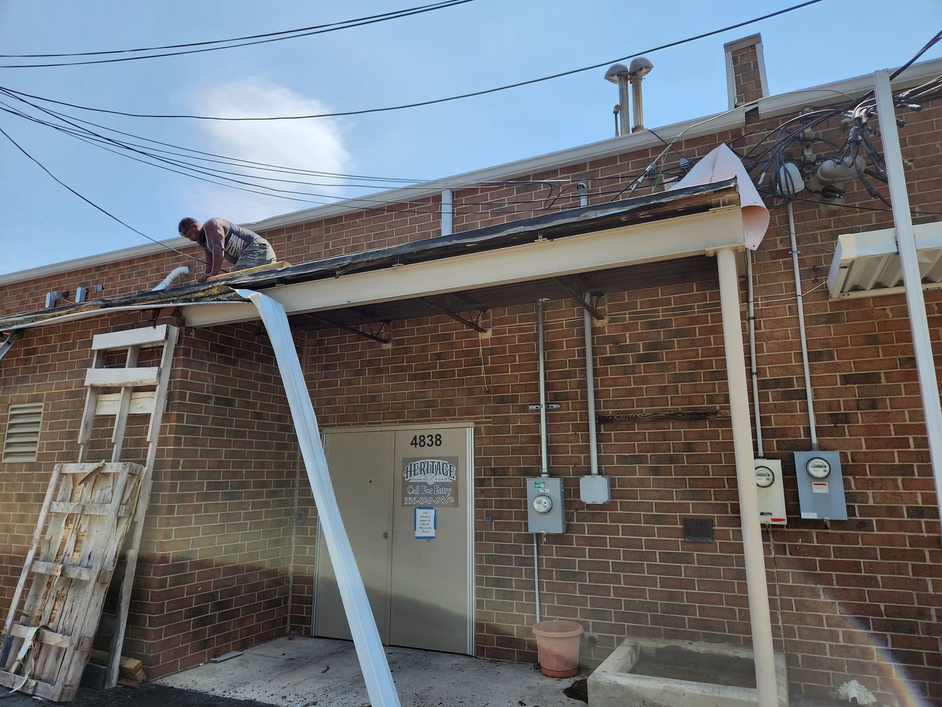Person on a roof installing guttering on a brick building with a ladder and electrical meters.