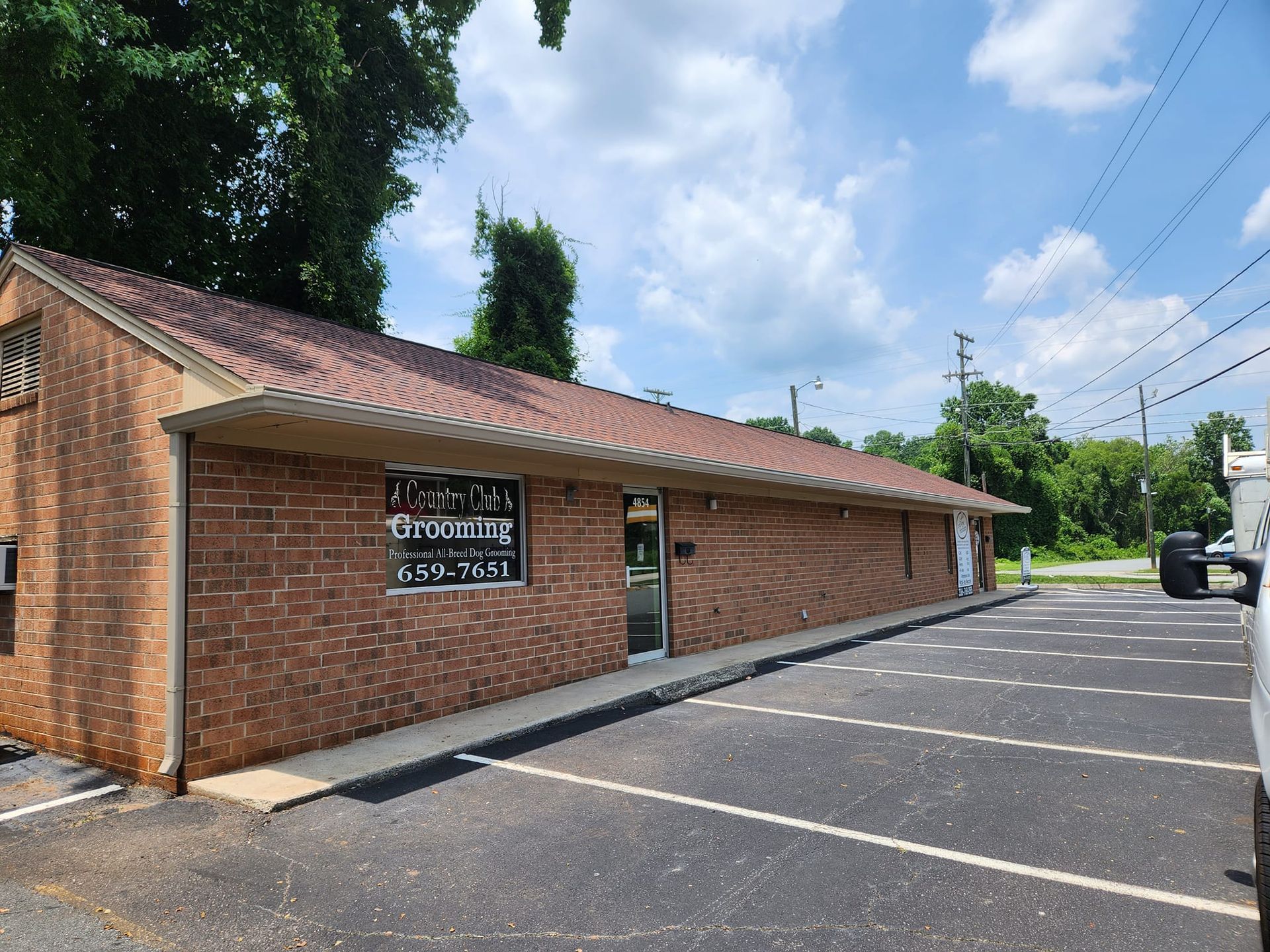 Brick building with a parking lot. Brown roof, door, and windows. Blue sky and trees in the background.