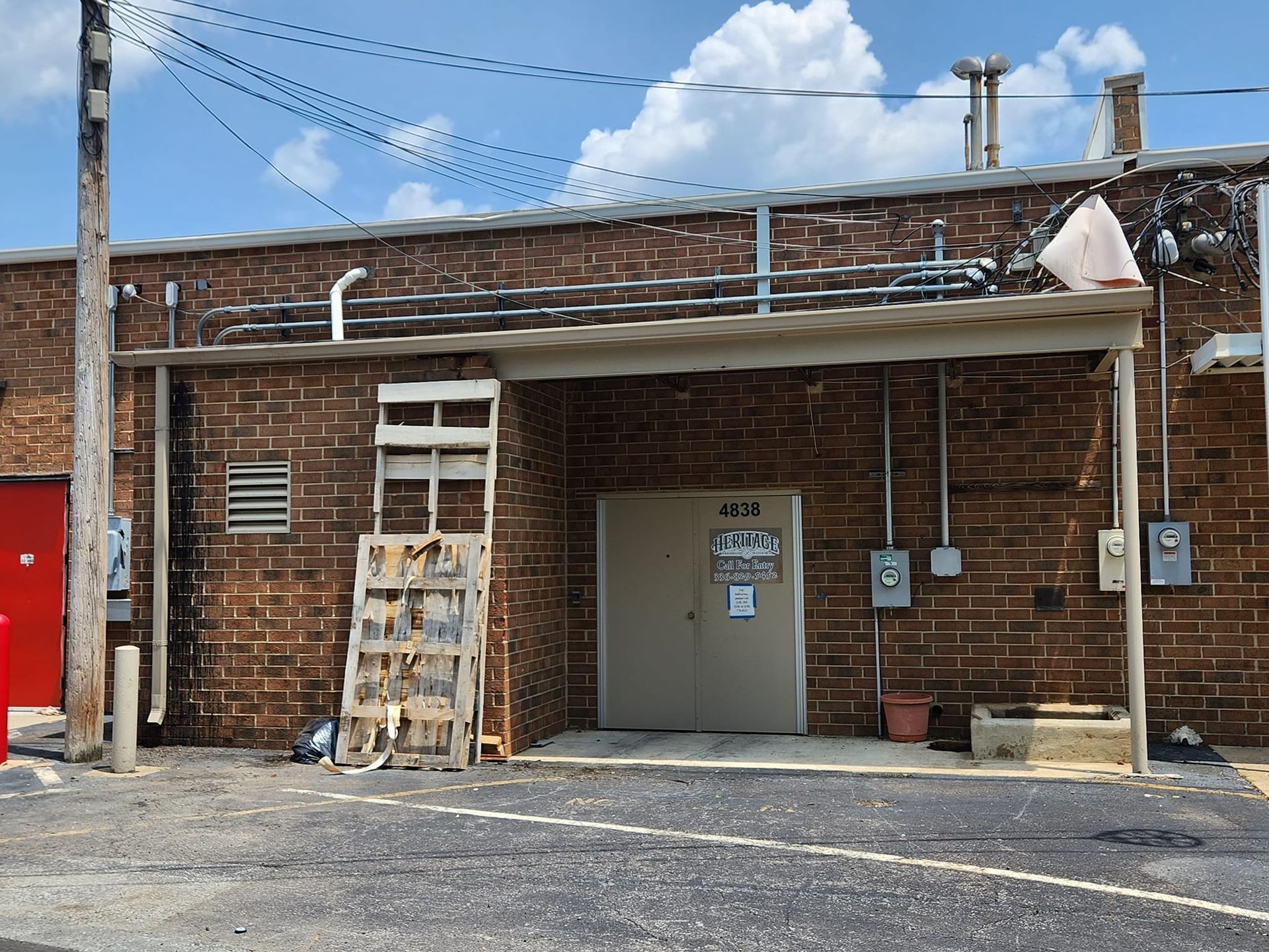 Brick building with a doorway and metal awning. A wooden structure leans against the wall.