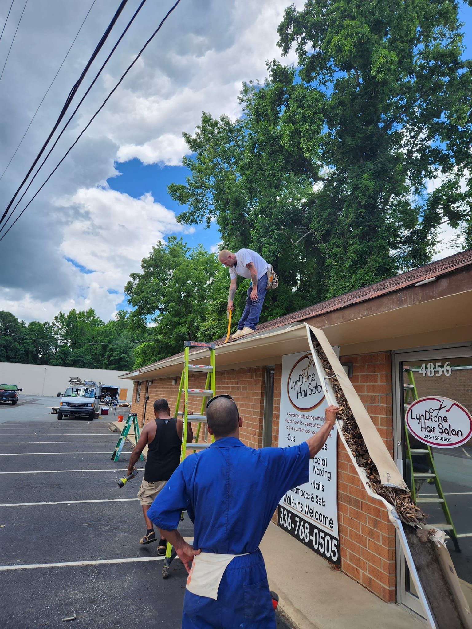 Construction workers repairing a building's roof and trim on a sunny day.