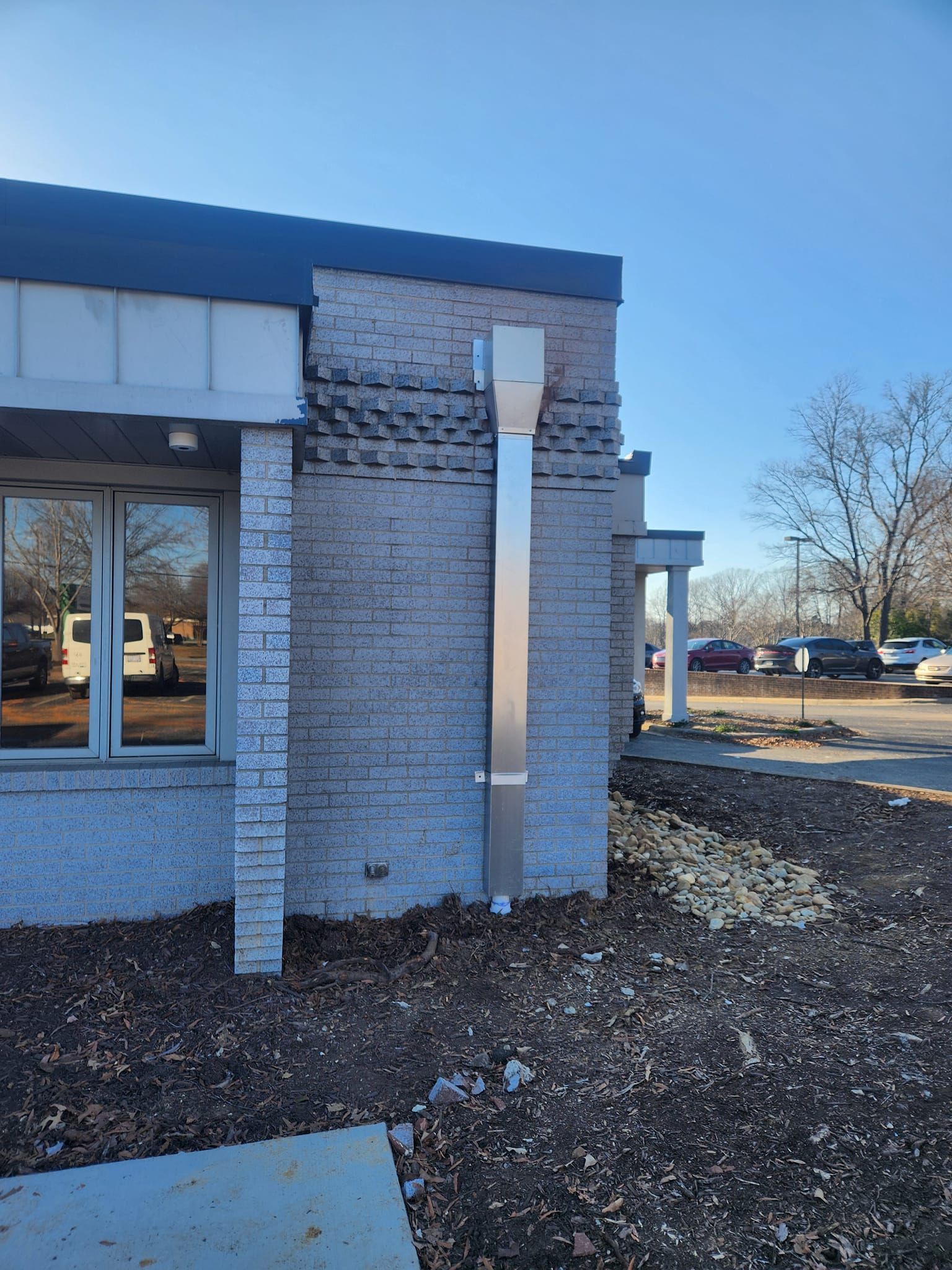Exterior view of a building with a large metal vent pipe attached to a brick wall. Sunny day.