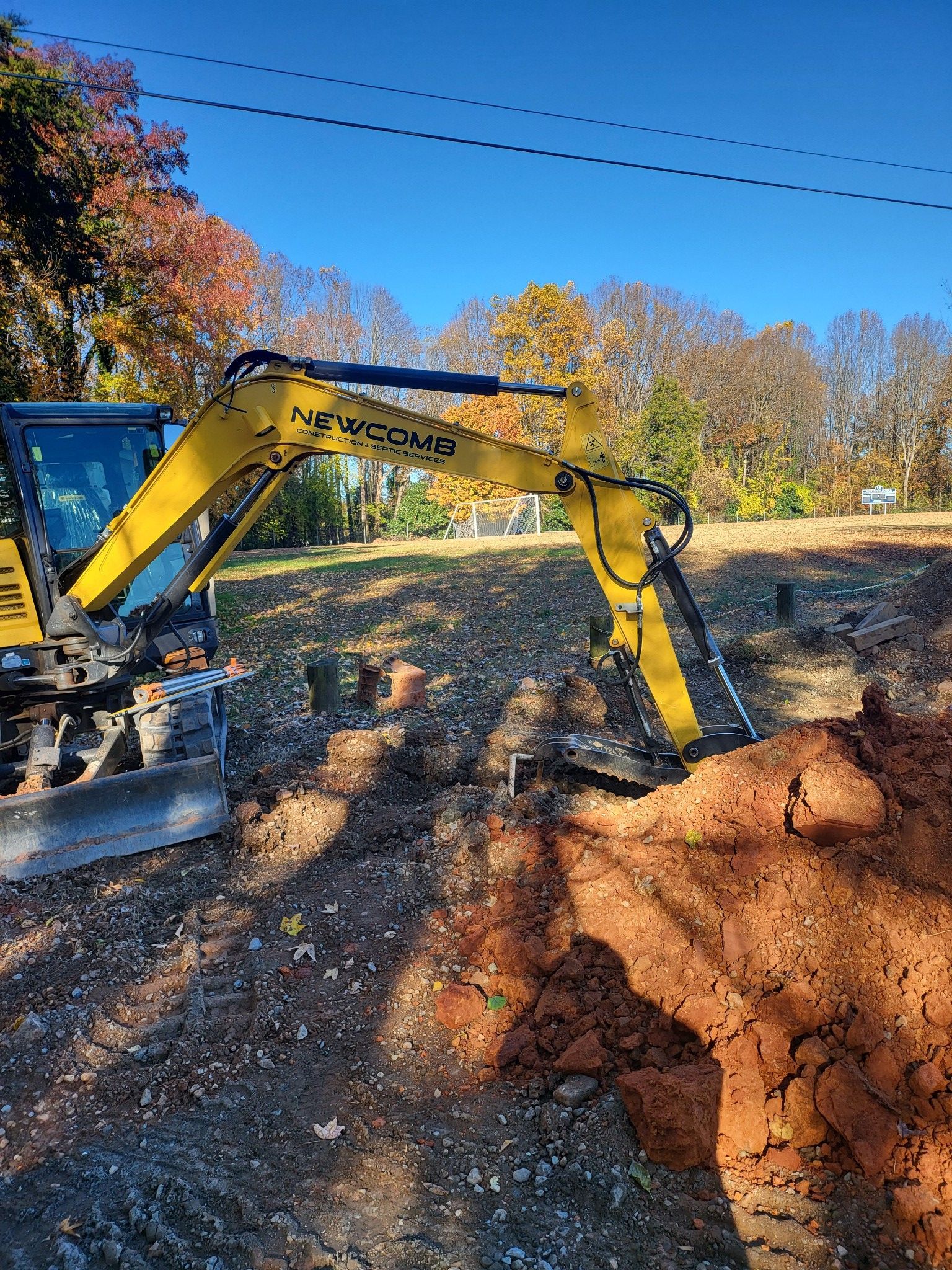 Yellow excavator digging into brown soil on a sunny day.