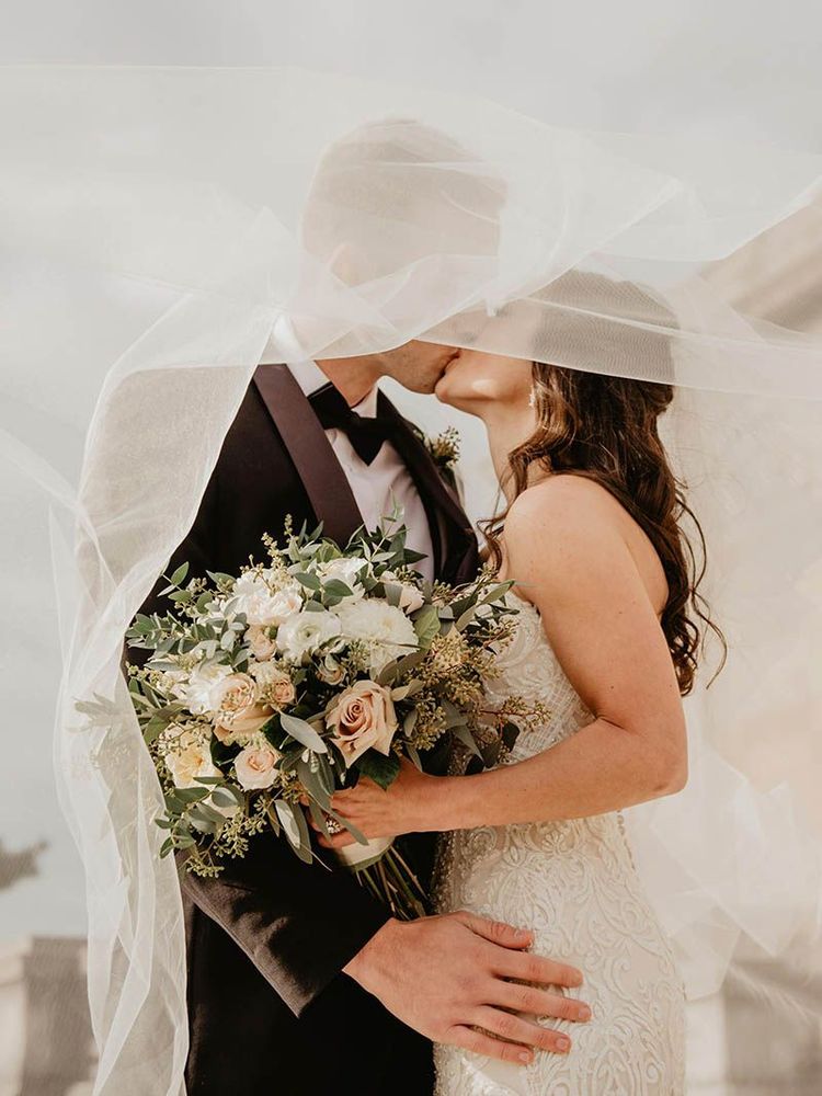 A bride and groom kissing under a veil on their wedding day.