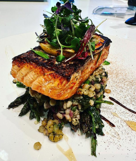 A piece of salmon with vegetables on top of it on a white plate