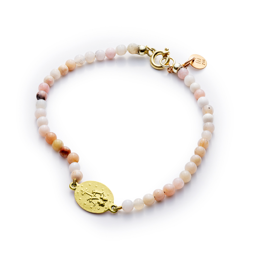 ein Armband mit rosa Perlen und einer Goldmünze auf weißem Hintergrund