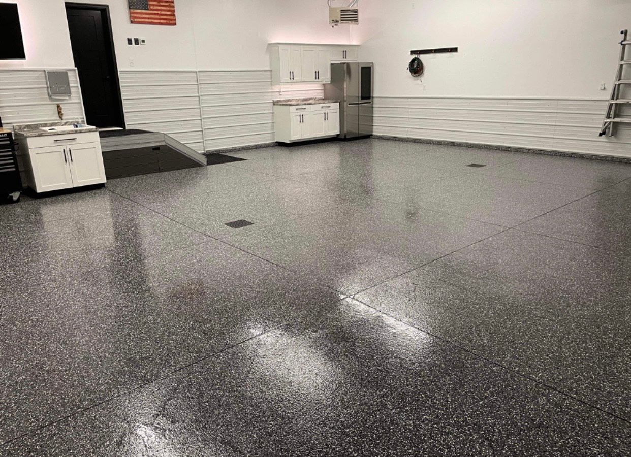 A large empty garage with a gray floor and white cabinets.