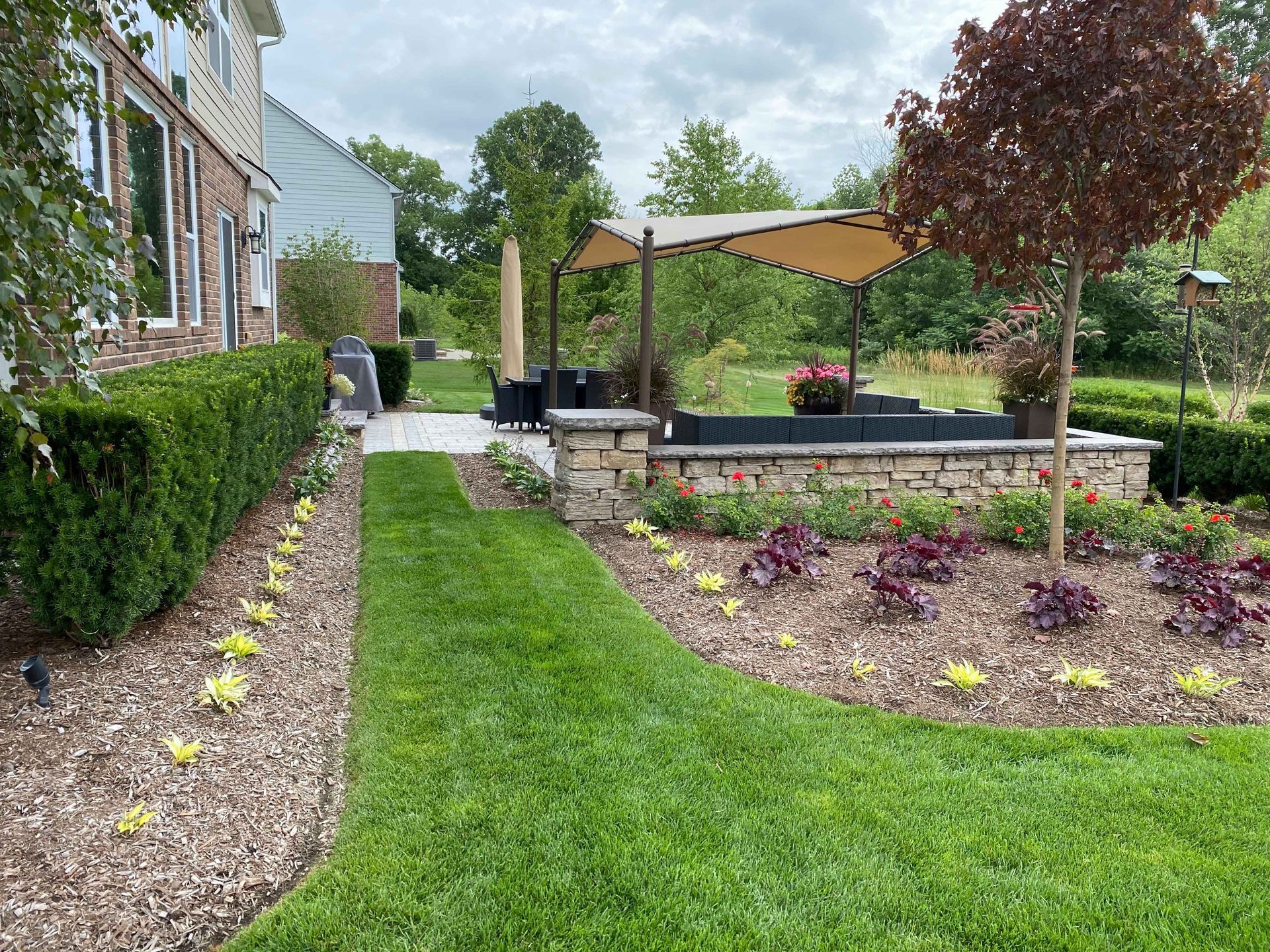 A lush green lawn with a patio and a canopy in the backyard of a house.