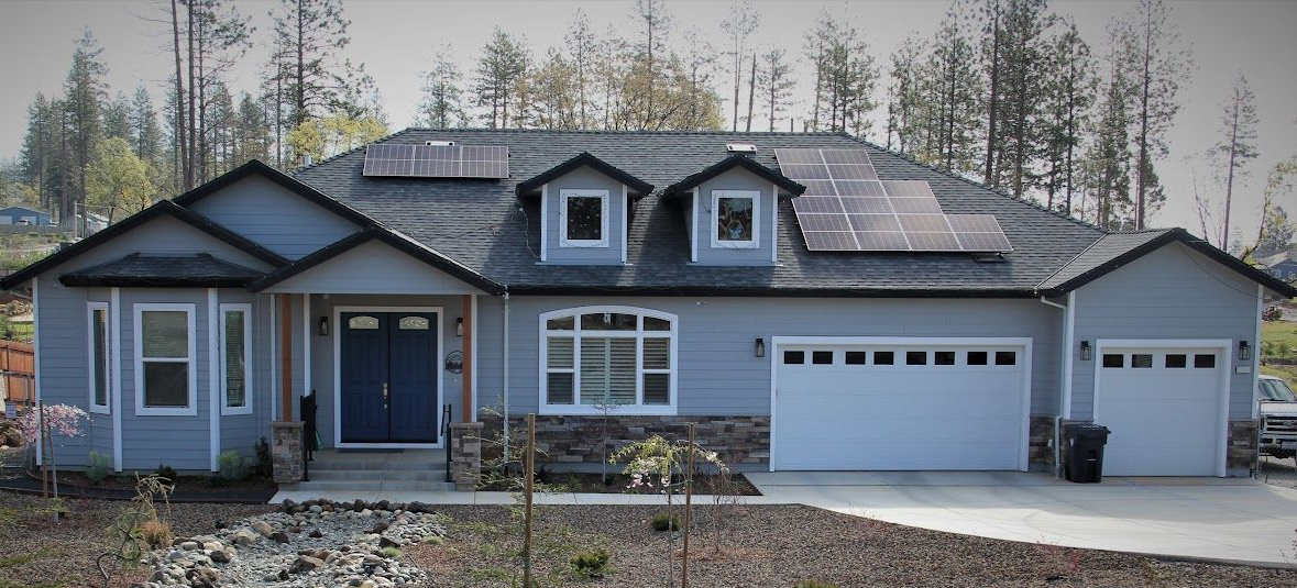 Light blue house with solar panels on the roof and white garage doors.
