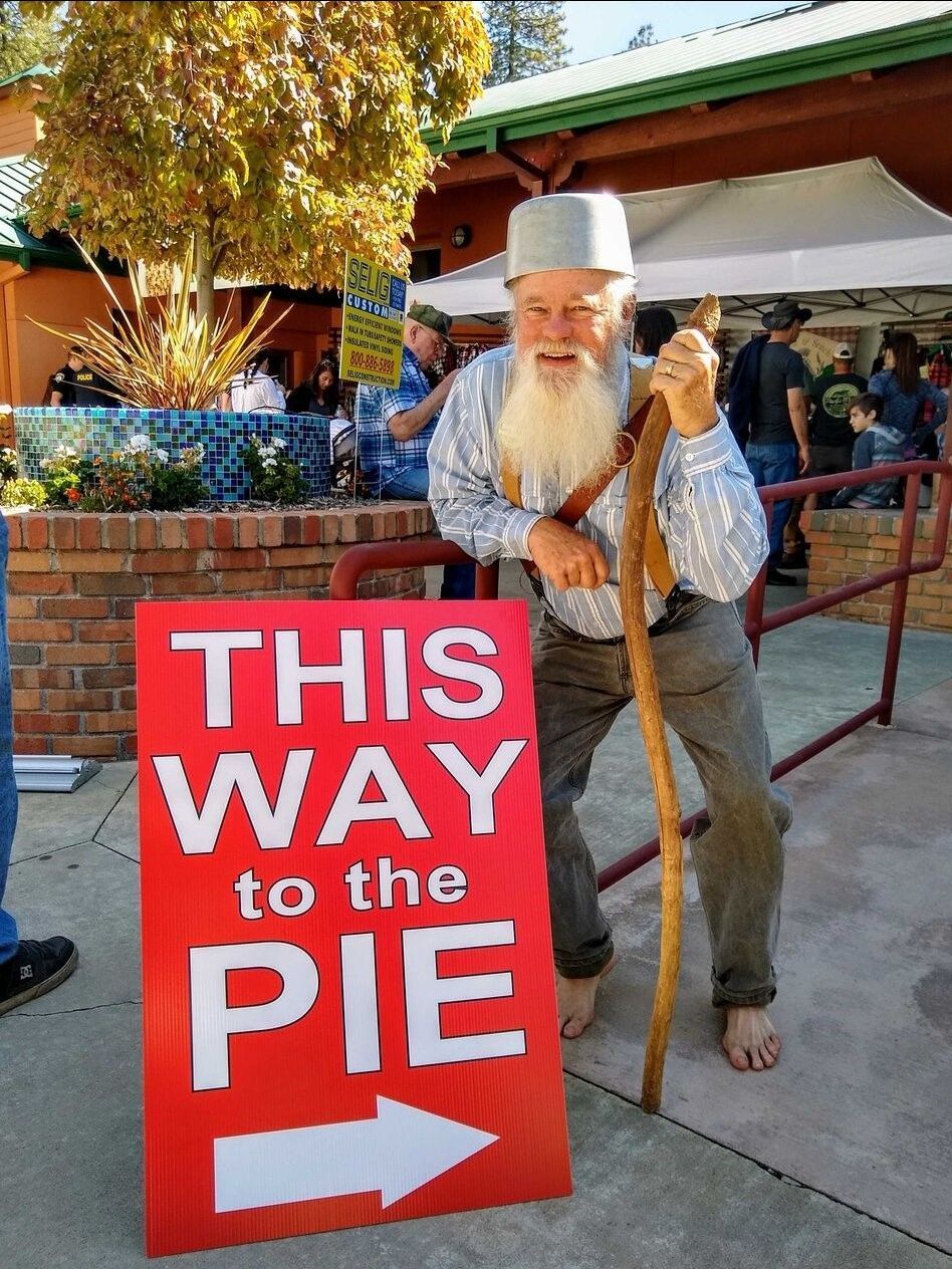 Smiling man in old-fashioned attire holds a sign that reads, 