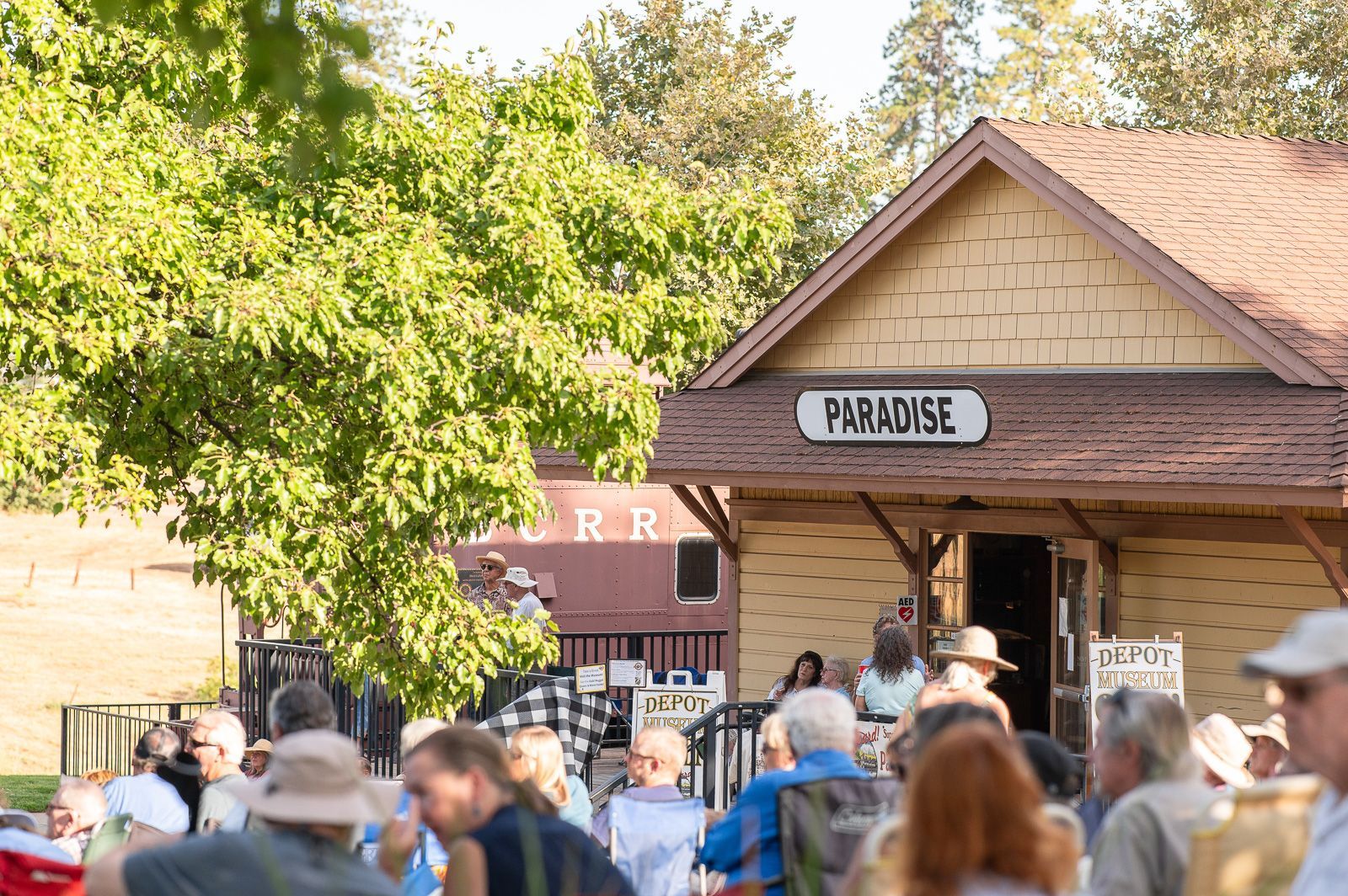 People gathered at the Paradise train station, likely an event. The station is light-colored with 