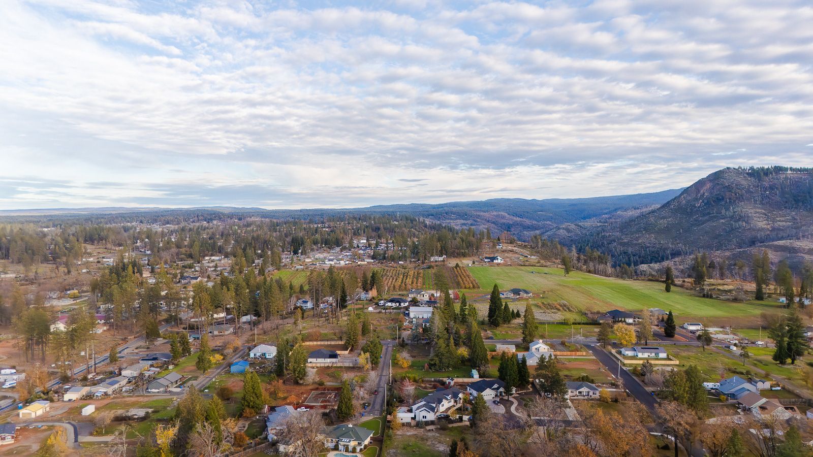 Aerial view of neighborhood in Paradise CA, with houses, trees, and fields under a cloudy sky.
