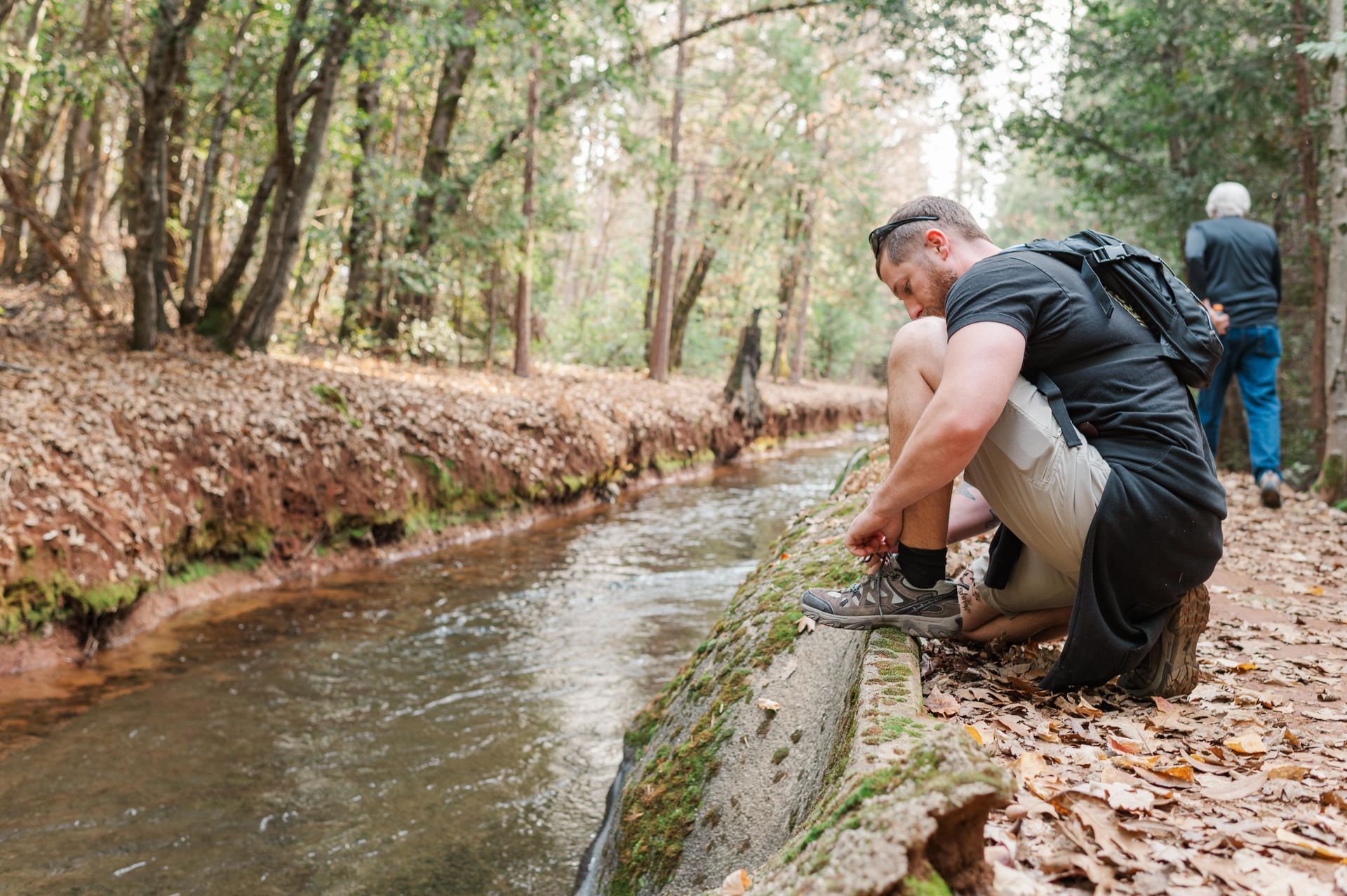 Man tying is shoe on a hiking trail near water
