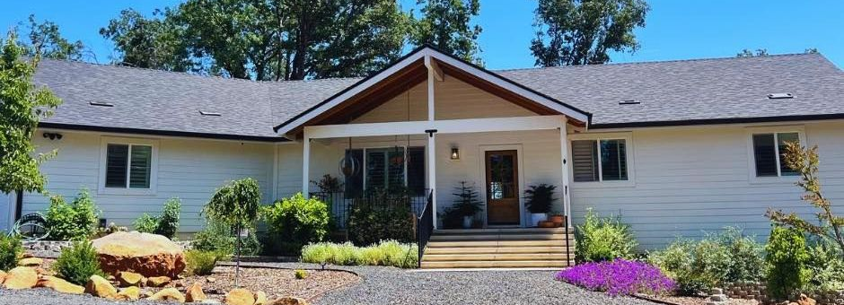Beige house with a covered porch and front landscaping, including a stone bed and purple flowers.