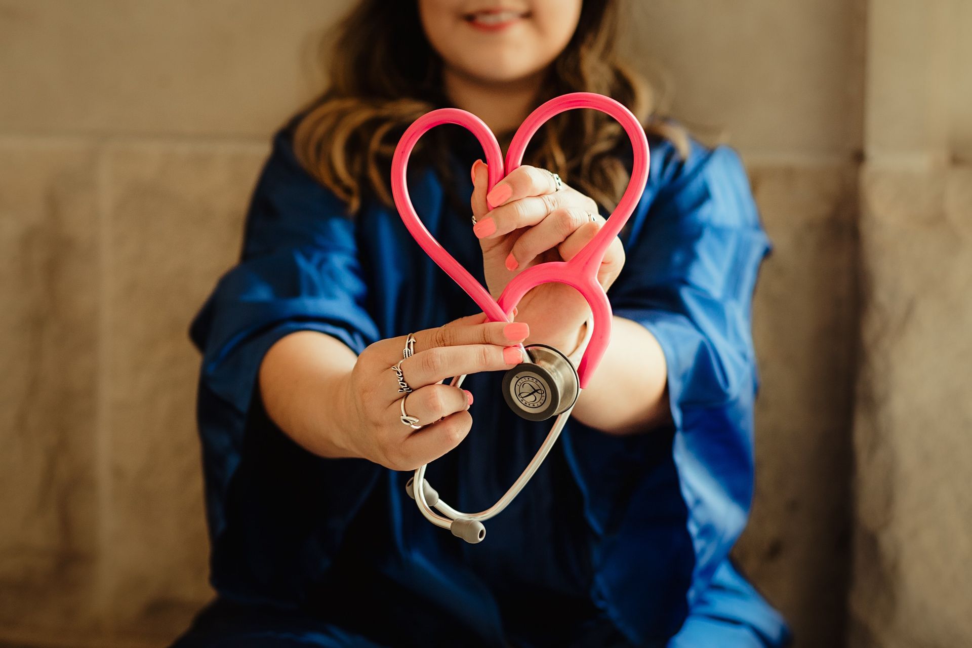 A woman is holding a pink stethoscope in the shape of a heart.