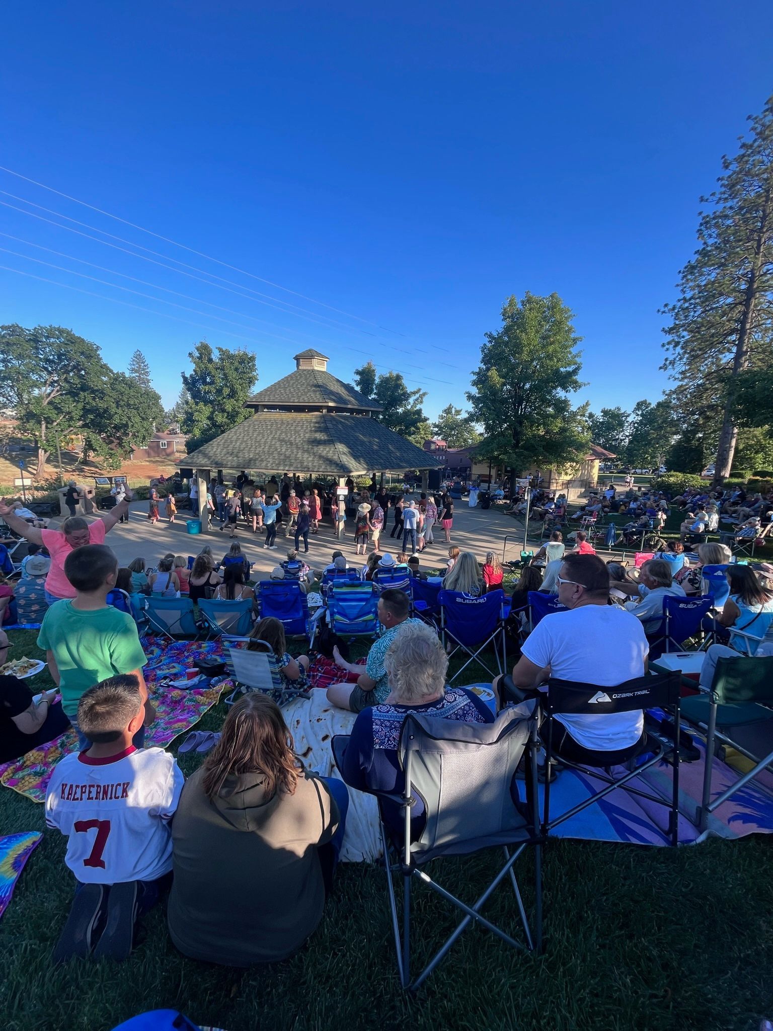 A group of people are sitting in chairs in a park watching a concert in Paradise and Magalia, California