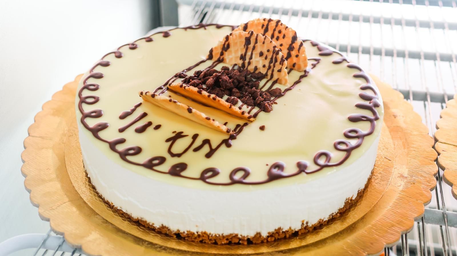 Una torta bianca con un pezzo di cioccolato sopra è appoggiata su un piatto di legno.