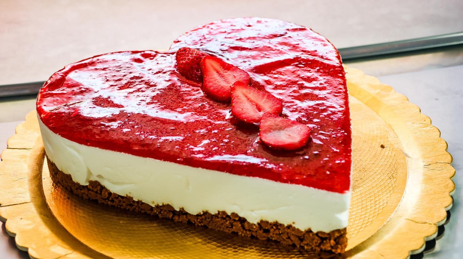 Su un piatto c'è una cheesecake a forma di cuore con delle fragole sopra.