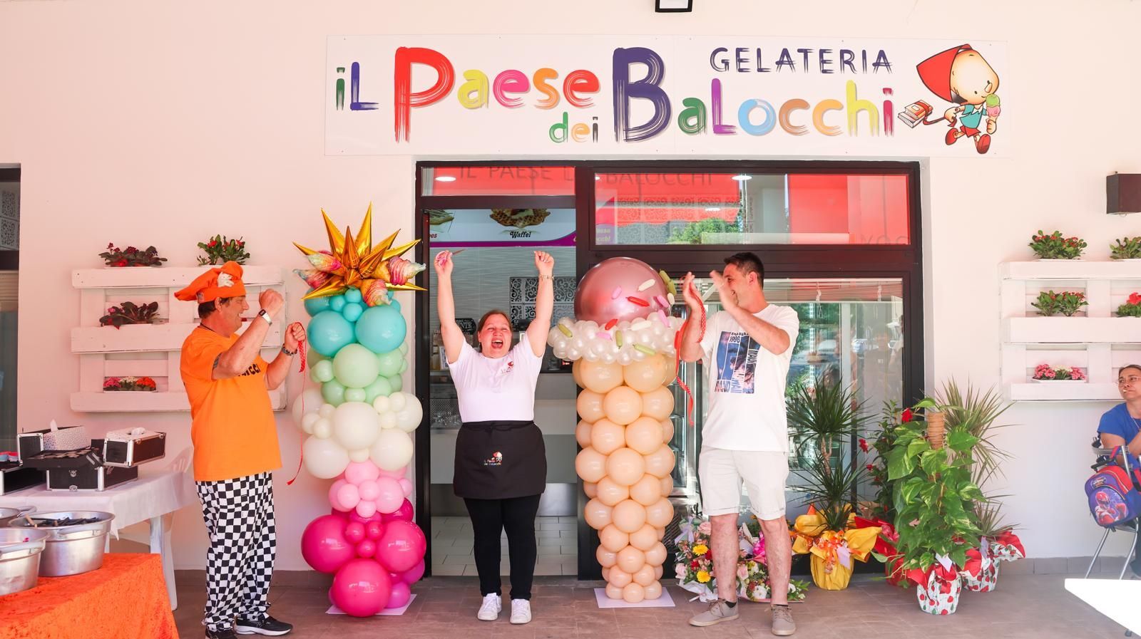 Un gruppo di persone è in piedi davanti a una gelateria decorata con palloncini.