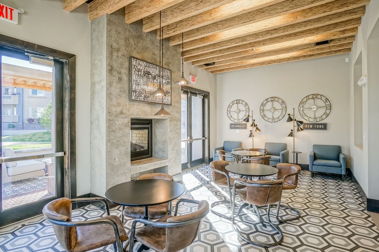 Communal lounge with round black tables, brown leather chairs, a fireplace, and geometric tile floor.