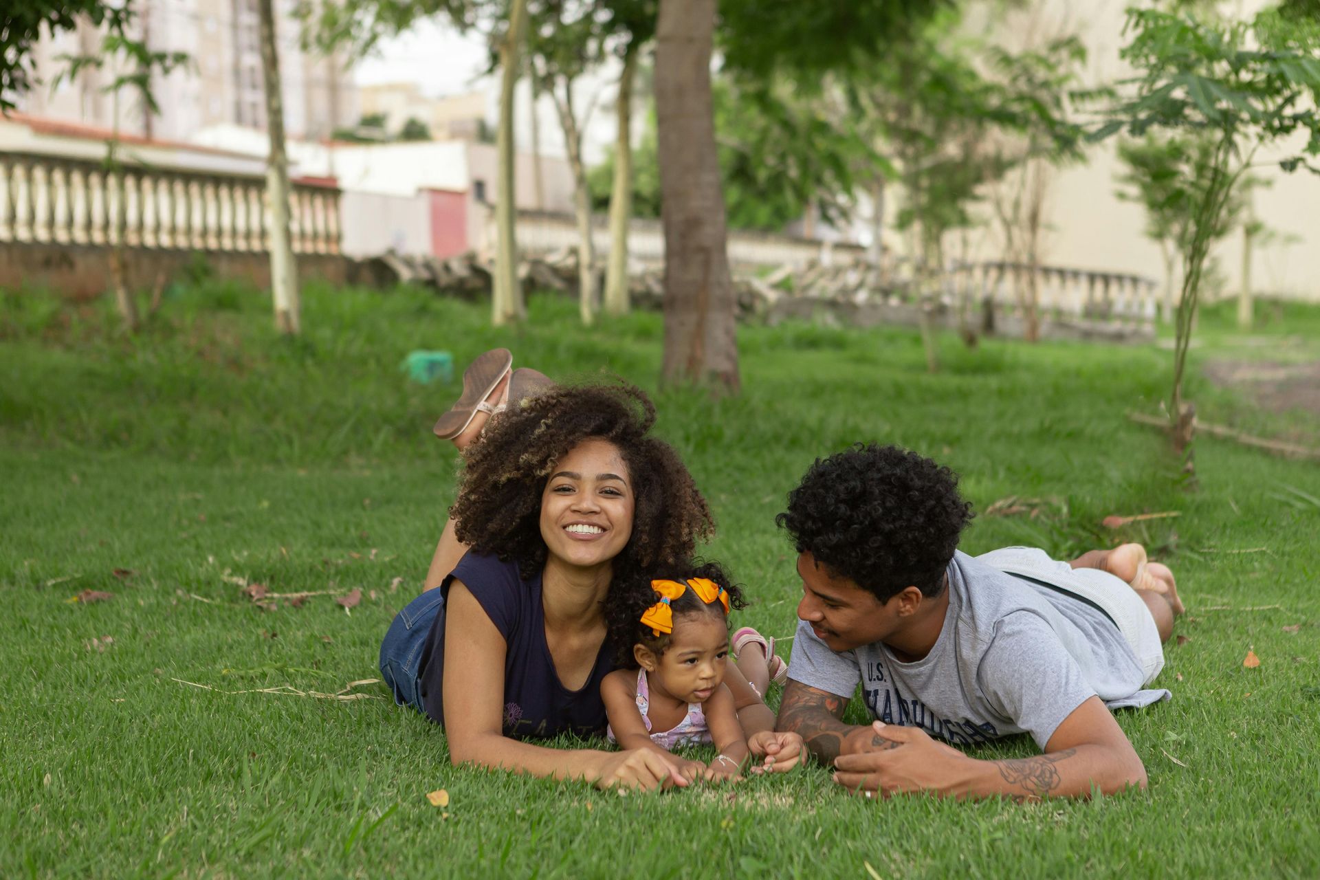 Family of three smiling while laying on grass in a park.