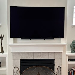 A large, black TV mounted above a white fireplace with a sound bar below. Built-in shelves flank the fireplace.