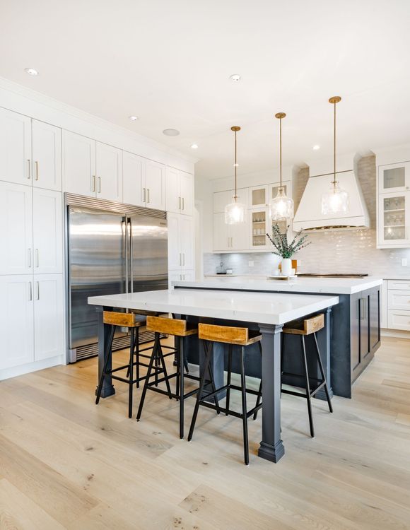 Modern kitchen with a large island and seating, stainless steel refrigerator, white cabinets, and light wood floors.