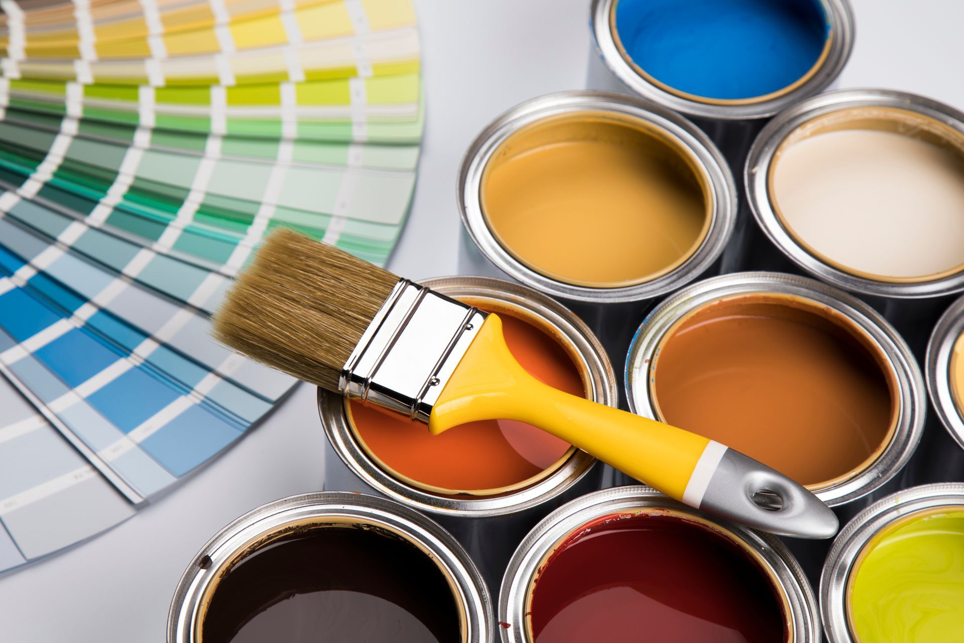 Paint cans with various colors, a paintbrush, and a color swatch fan.