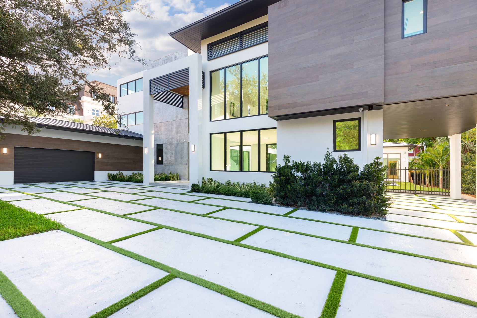 Modern white house with gray accents, large windows, and a driveway with grass between rectangular concrete slabs.