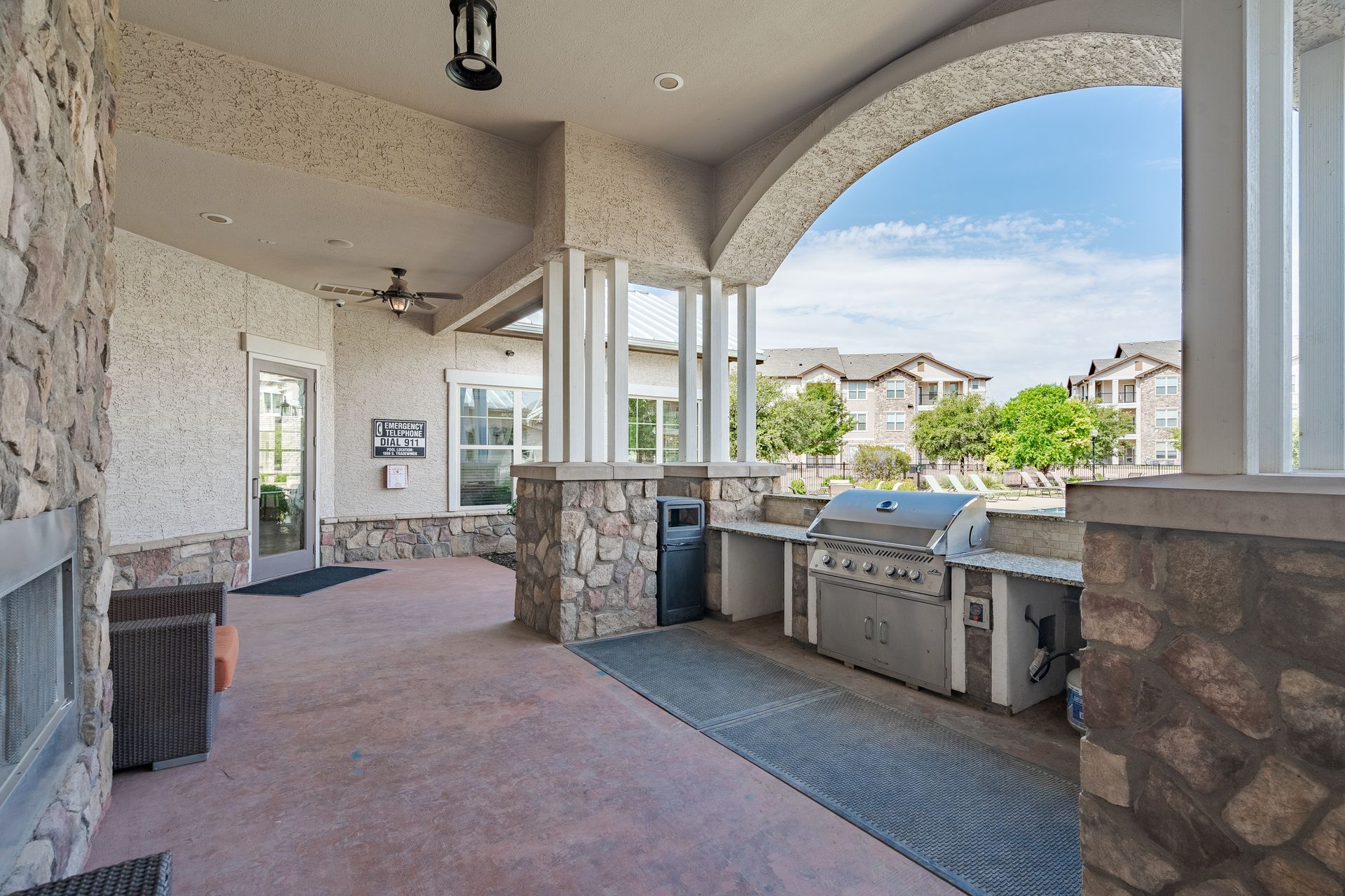 Outdoor communal grilling area under a covered patio with stone columns and a built-in grill.