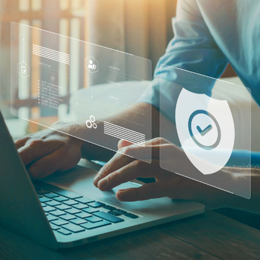 Hands typing on a laptop with a transparent cybersecurity shield and checkmark overlay