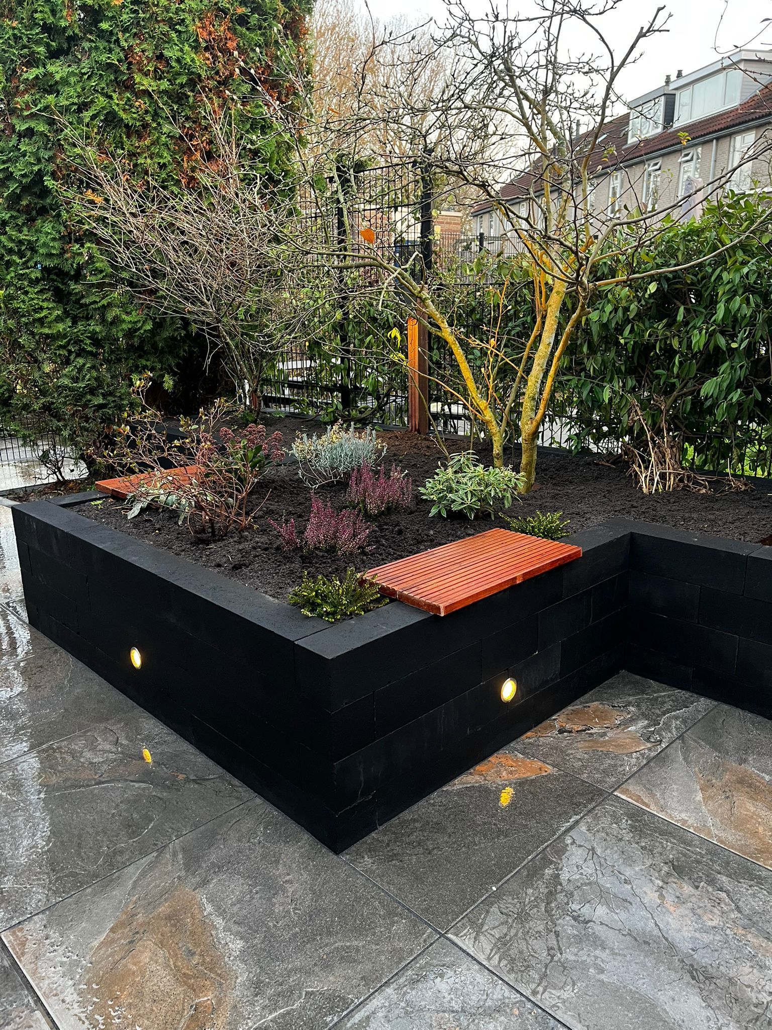 Zwarte, verhoogde plantenbak met planten, oranje accenten en ingebouwde verlichting op een stenen terras.
