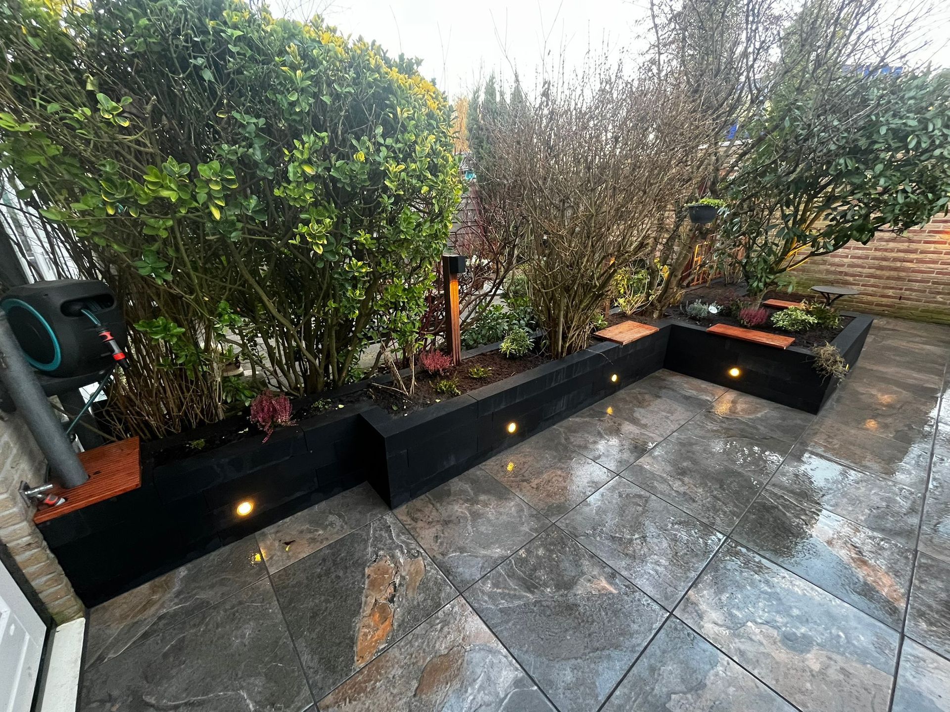 Verhoogde plantenbedden met zwarte frames en ingebouwde verlichting, gevuld met groene struiken, op een stenen terras.