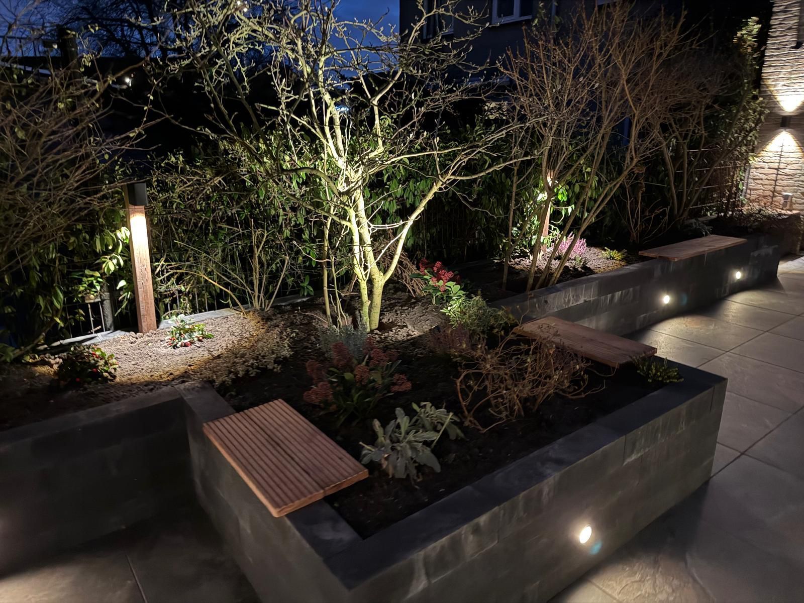 Buitenperk met banken, verlicht door spotjes. Planten en bomen worden 's nachts verlicht.