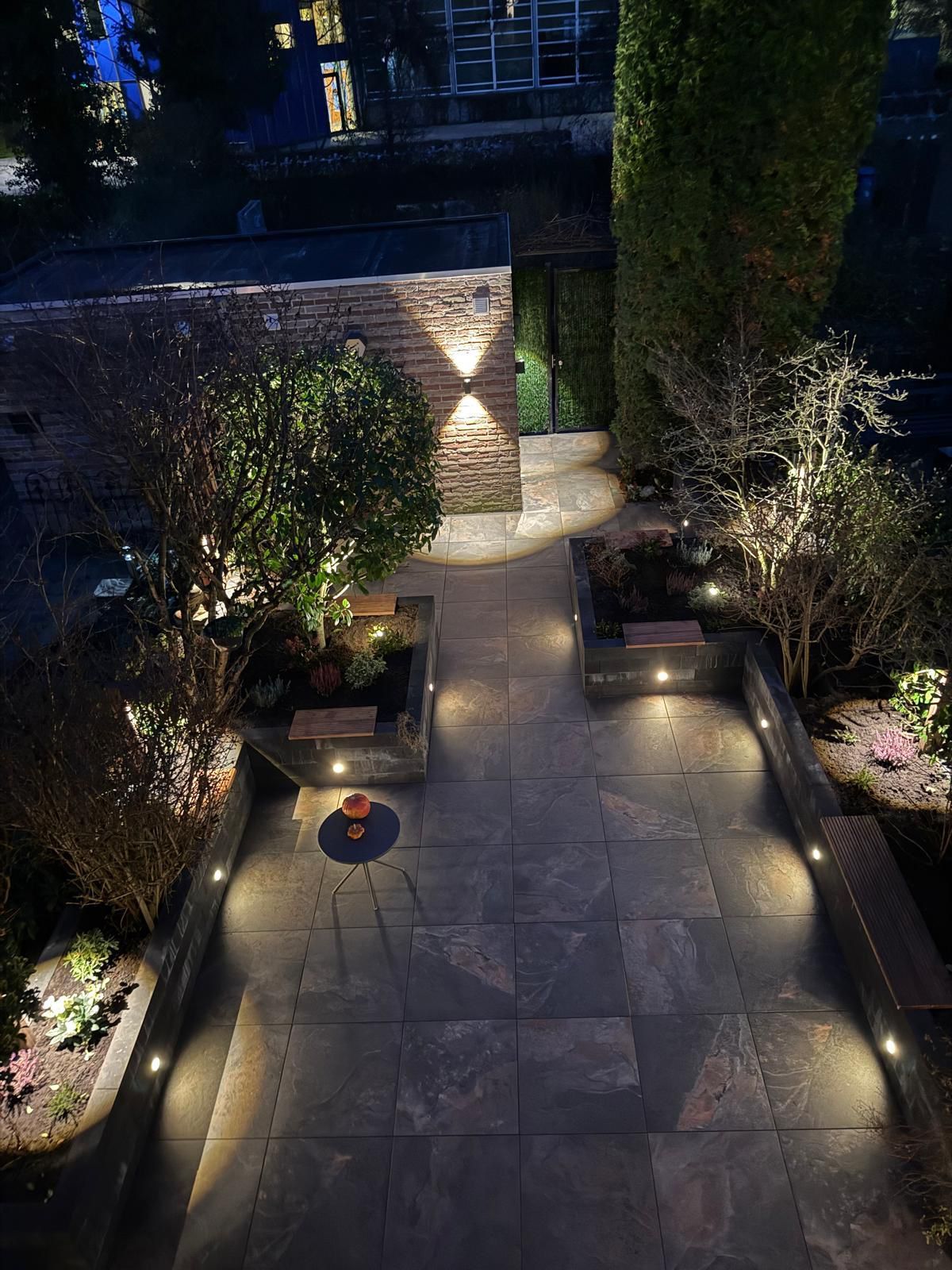 Pad met verlichte plantenbakken en muur. Donkere steen, nacht, warme verlichting.