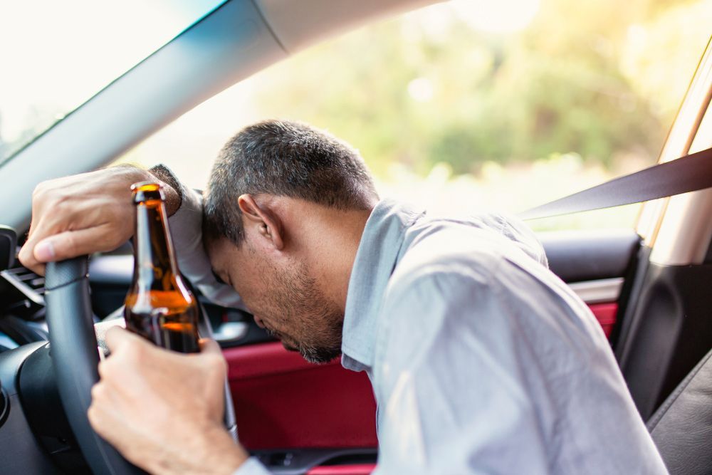 A Man Is Sleeping In A Car While Holding A Bottle Of Beer — David Tamanika Solicitors in Ballarat Central, VIC