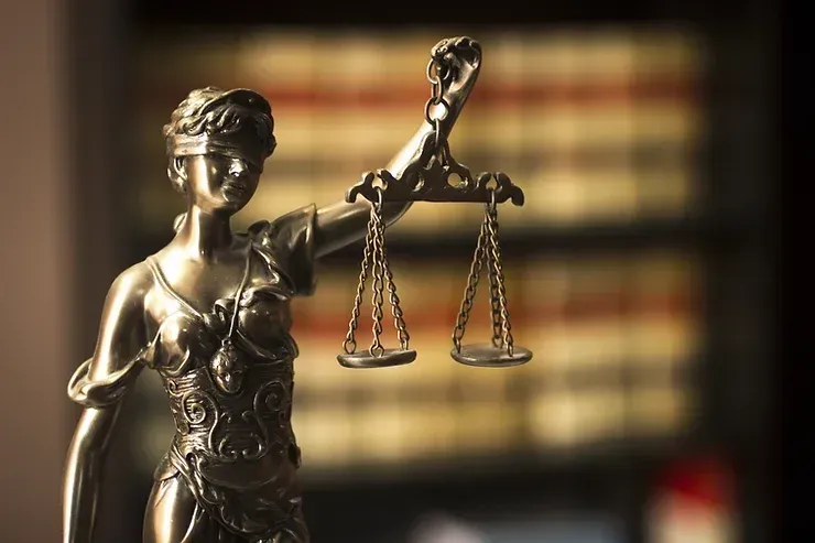 A Statue Of Justice Holding A Pair Of Scales In Front Of A Bookshelf — David Tamanika Solicitors in Ararat, VIC