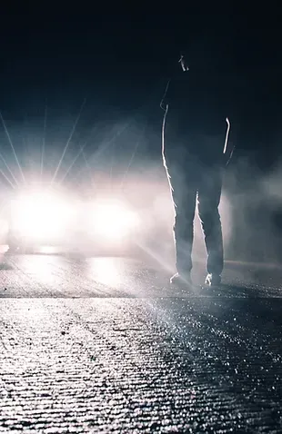 A Person Is Walking Down A Street At Night In Front Of A Car — David Tamanika Solicitors in Ararat, VIC