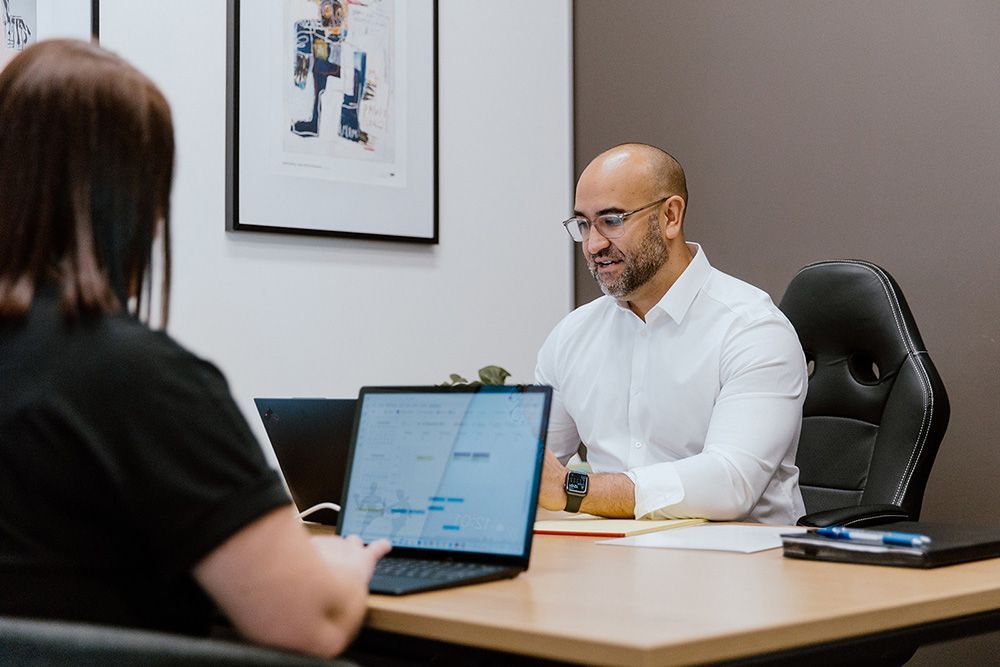 A Man And A Woman Are Sitting At A Table With A Laptop — David Tamanika Solicitors in Ballarat Central, VIC
