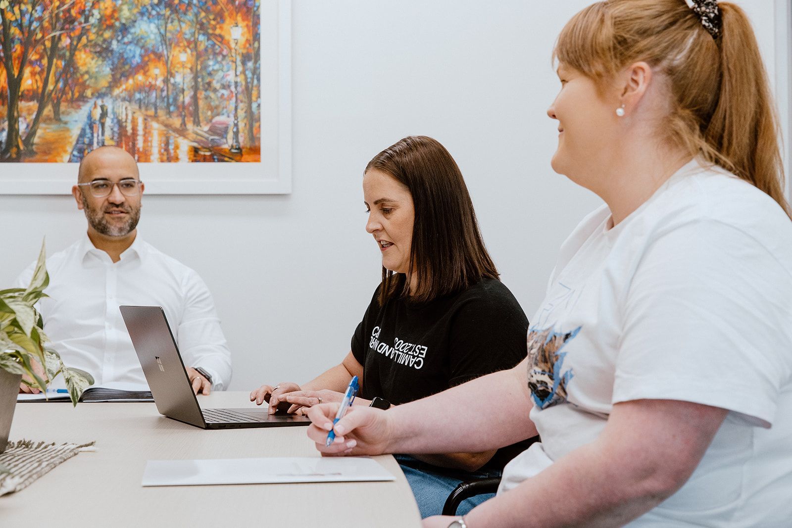 A Man And Two Women Are Sitting At A Table With A Laptop — David Tamanika Solicitors in Ballarat Central, VIC