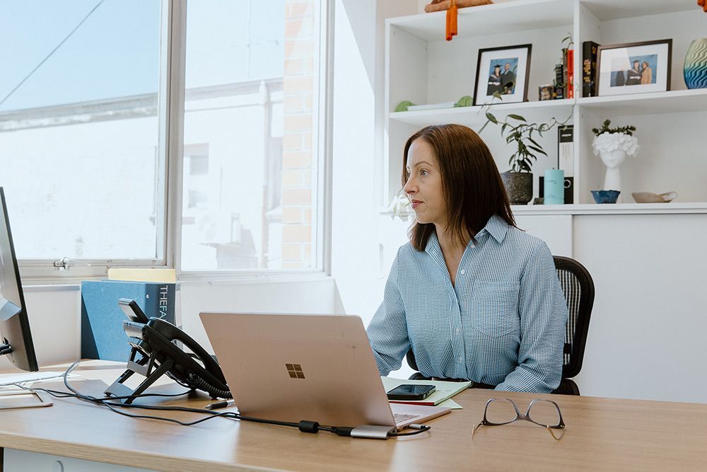 A Woman Is Sitting At A Desk Using A Laptop Computer — David Tamanika Solicitors in Bacchus Marsh, VIC