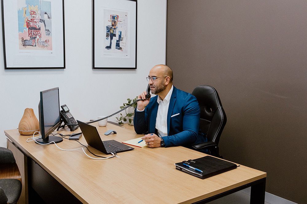 A Man In A Blue Suit Is Sitting At A Desk Talking On A Phone — David Tamanika Solicitors in Ararat, VIC
