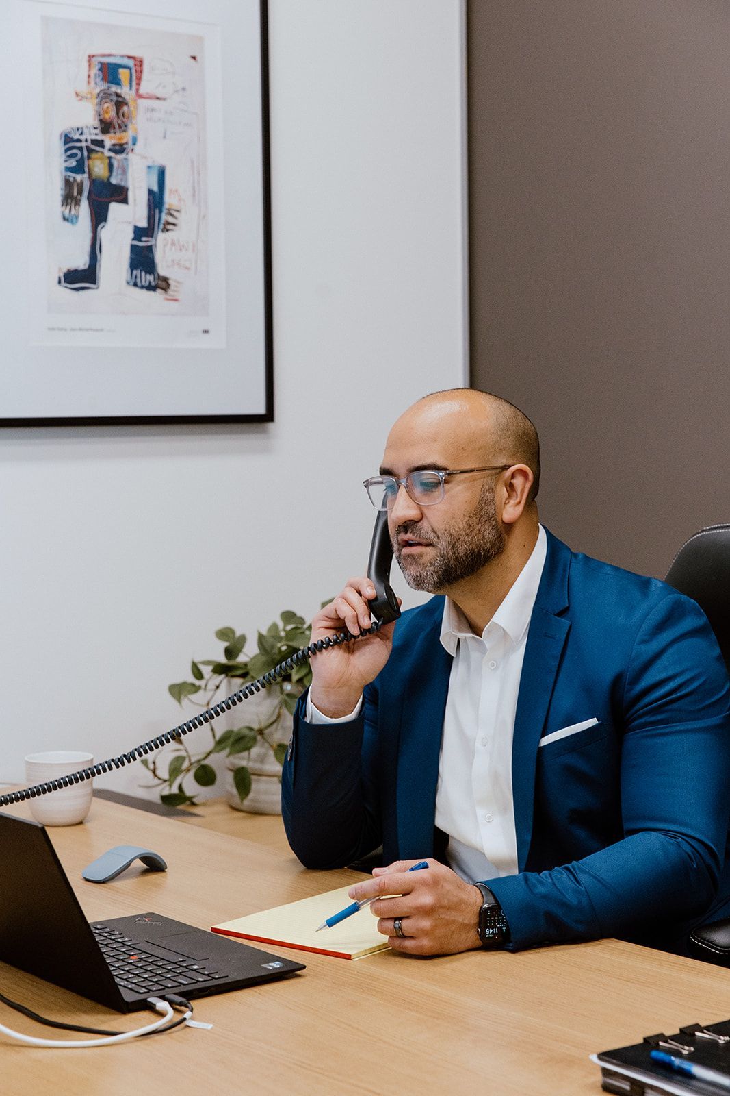 A Man Is Sitting At A Desk Talking On A Tele Phone — David Tamanika Solicitors in Ballarat Central, VIC