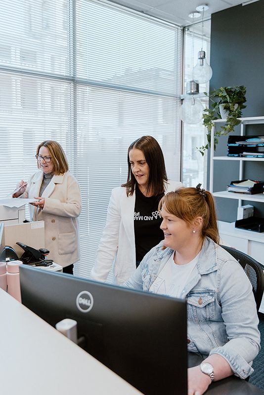 A Group Of Women Are Standing Around A Computer In An Office — David Tamanika Solicitors in Ararat, VIC