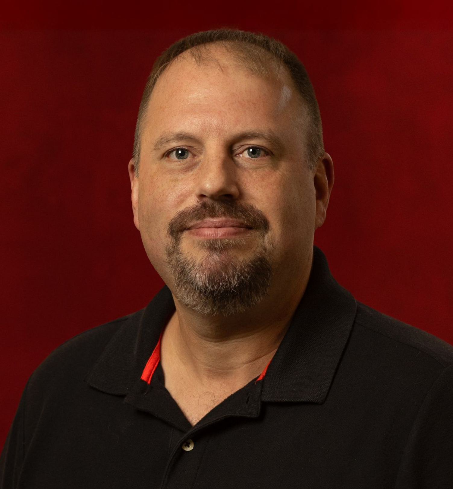 A man with a beard is wearing a red shirt and smiling