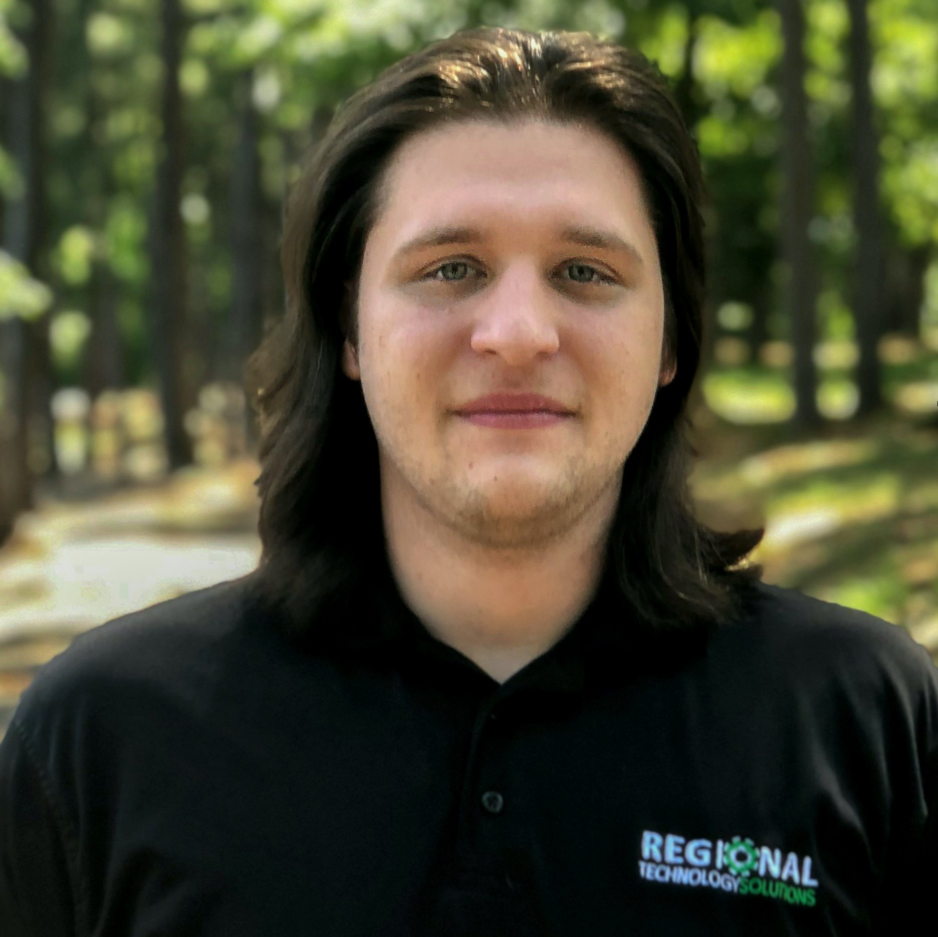 A young man with long hair is wearing a black shirt that says regional technology solutions.