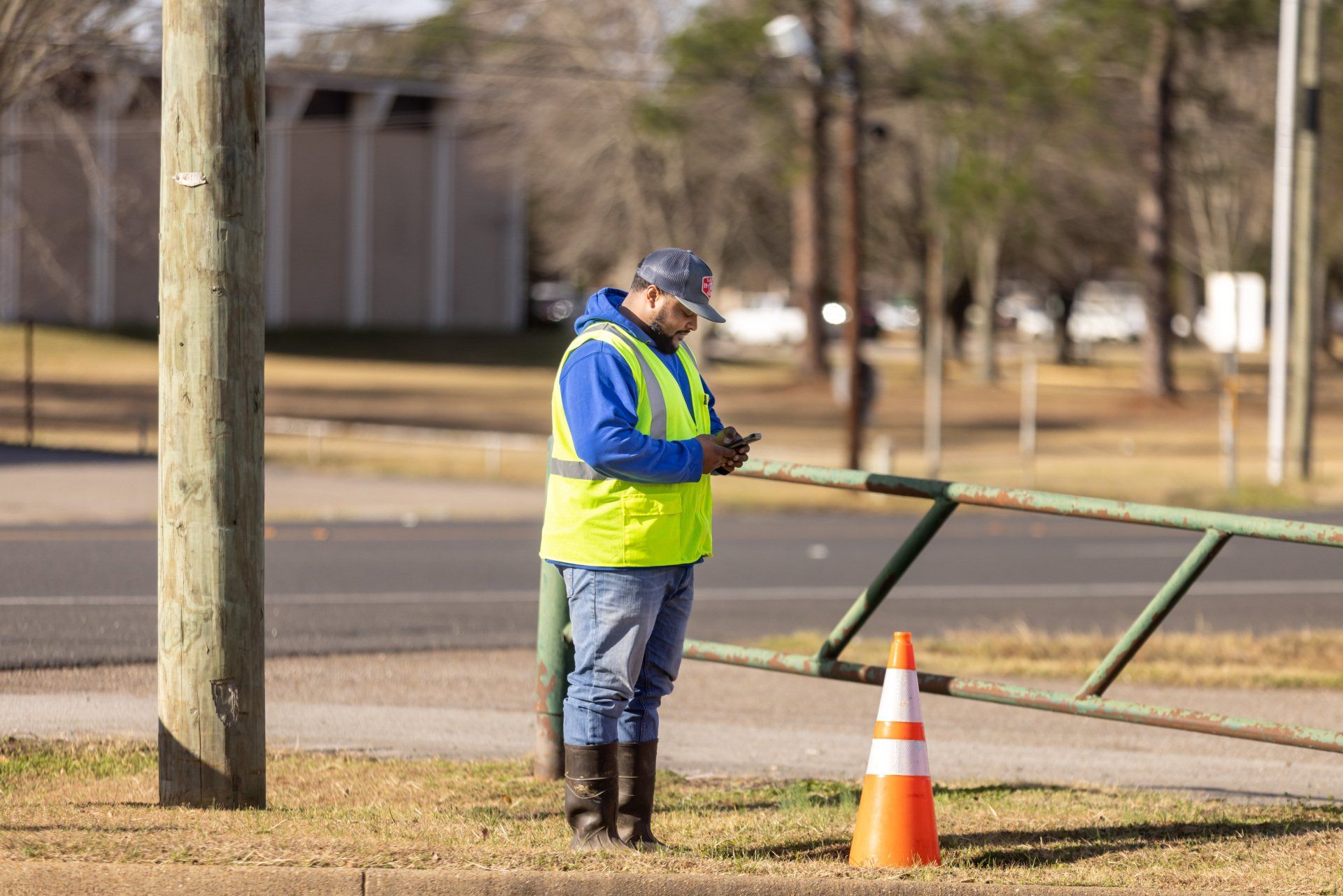 Man wearing blue hoodie and yellow vest standing outside staring at his phone