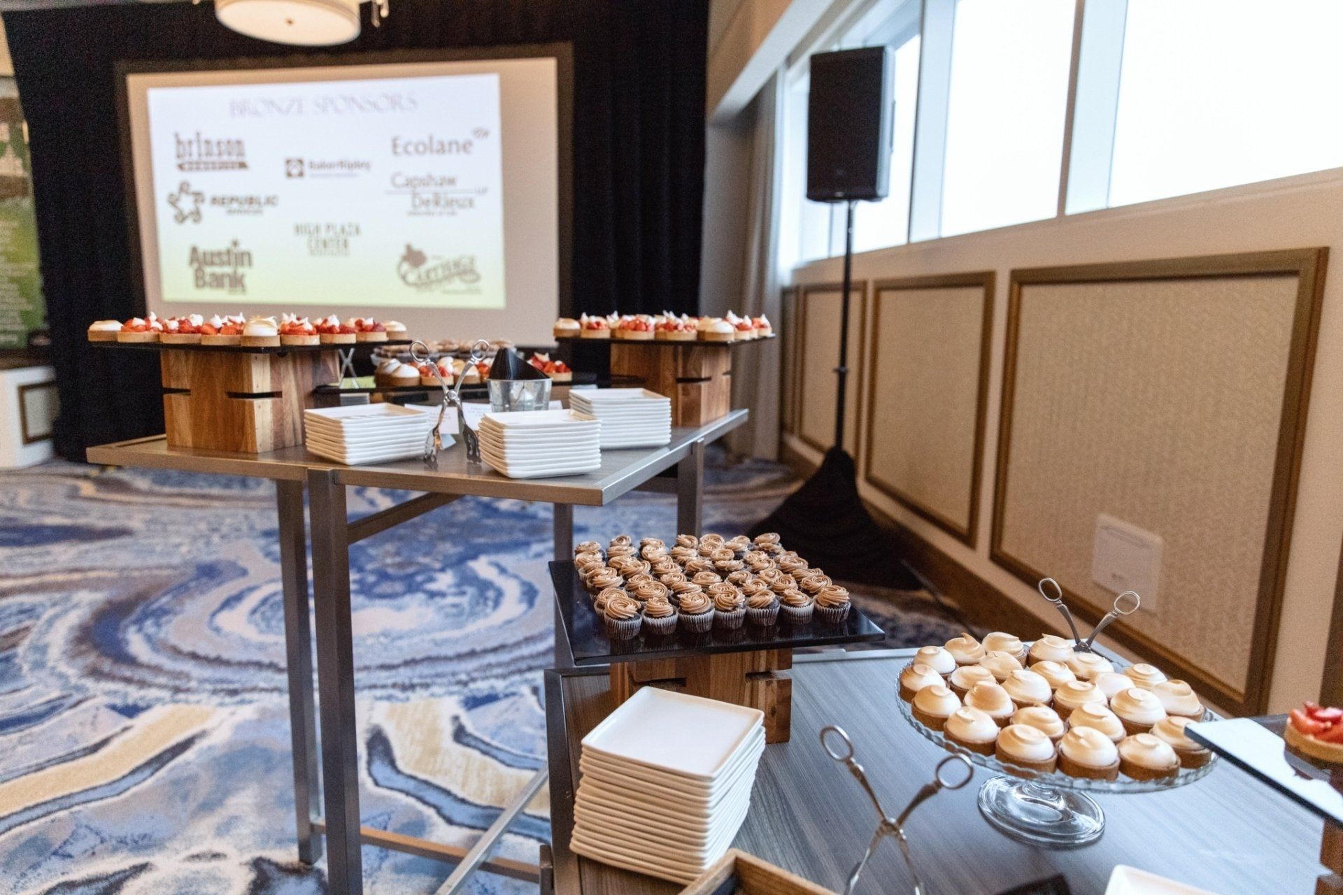 A buffet table with cupcakes and a projector screen in the background.