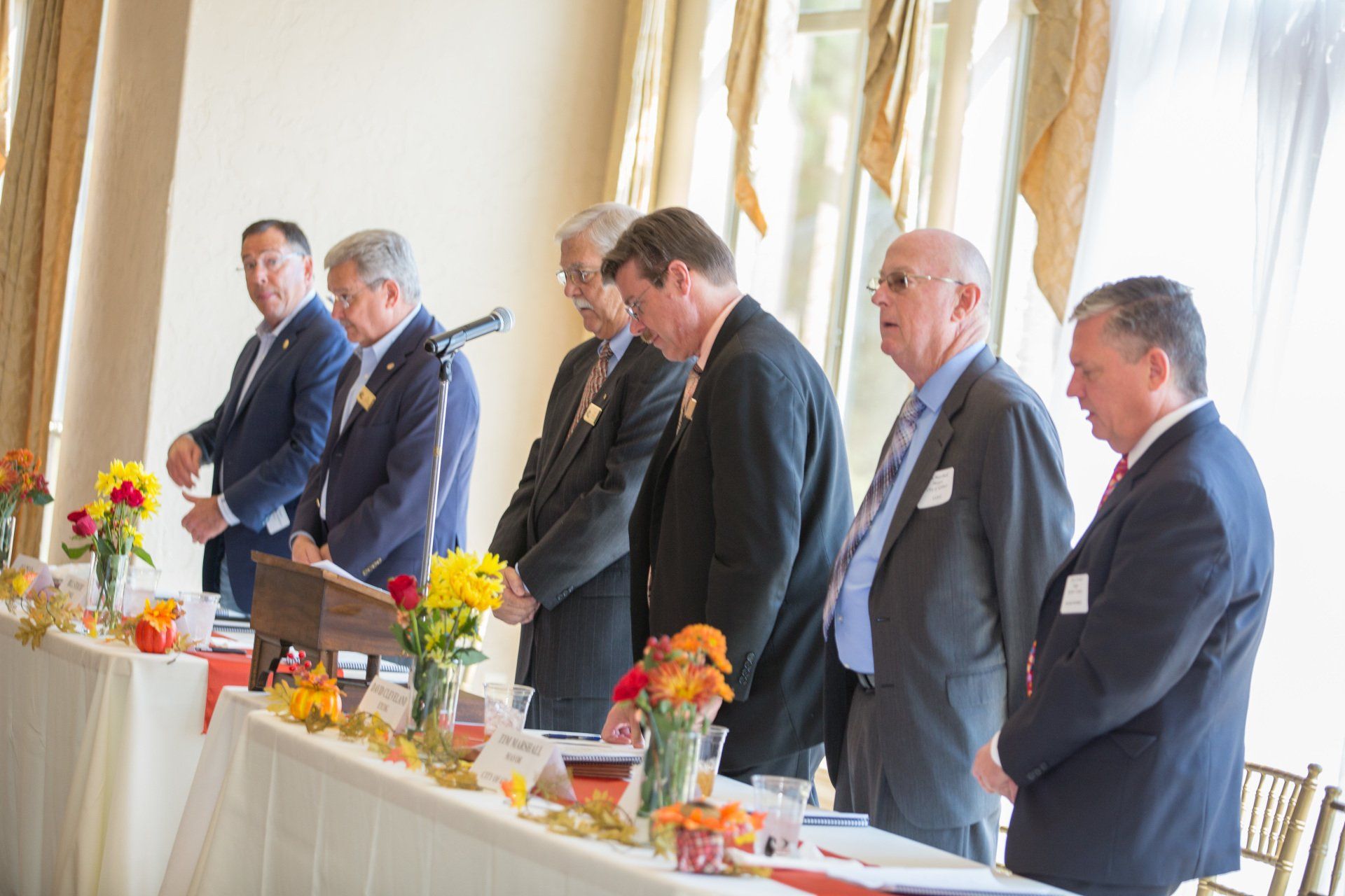 A group of men in suits are standing in front of a long table.