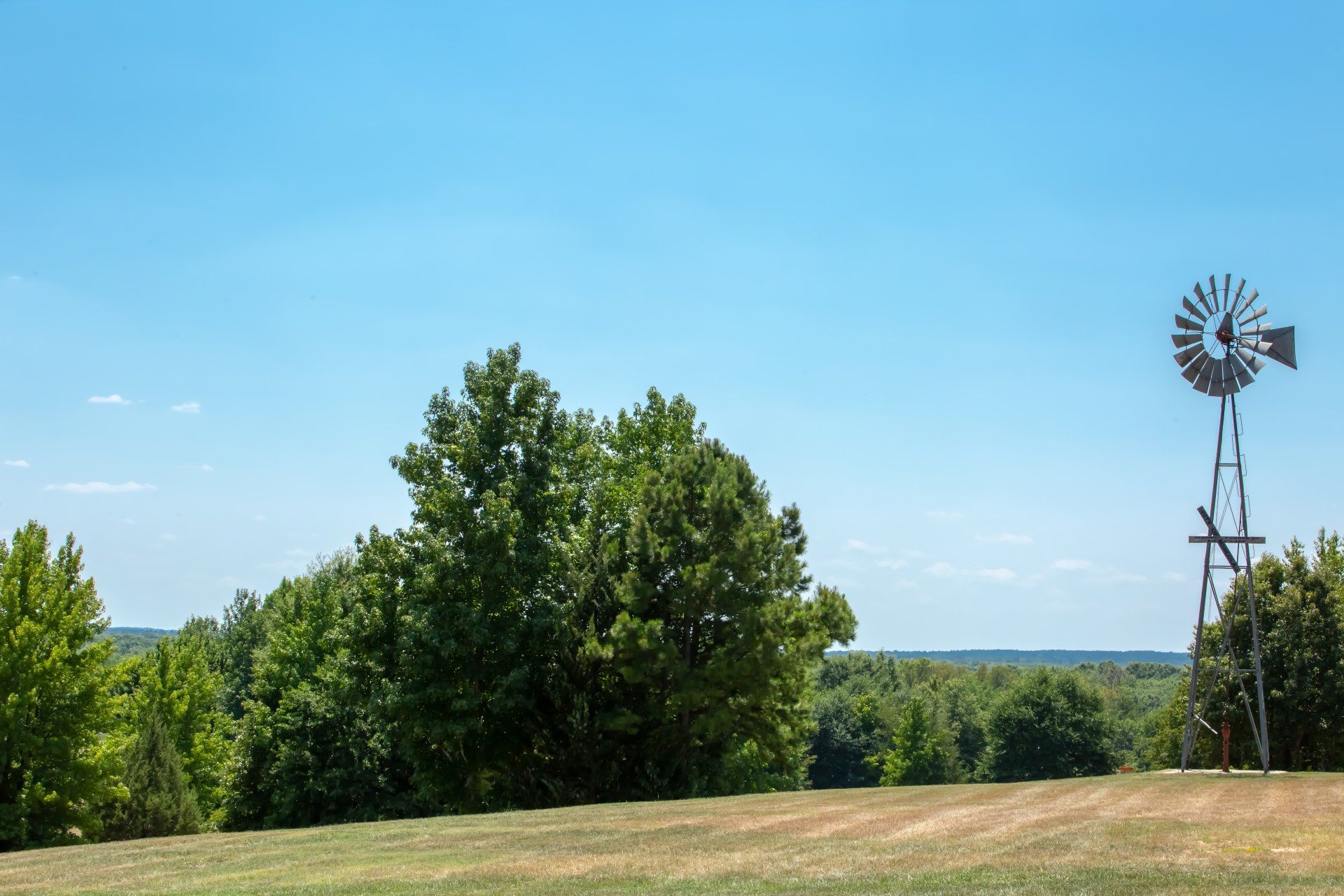 A windmill is sitting in the middle of a grassy field surrounded by trees.